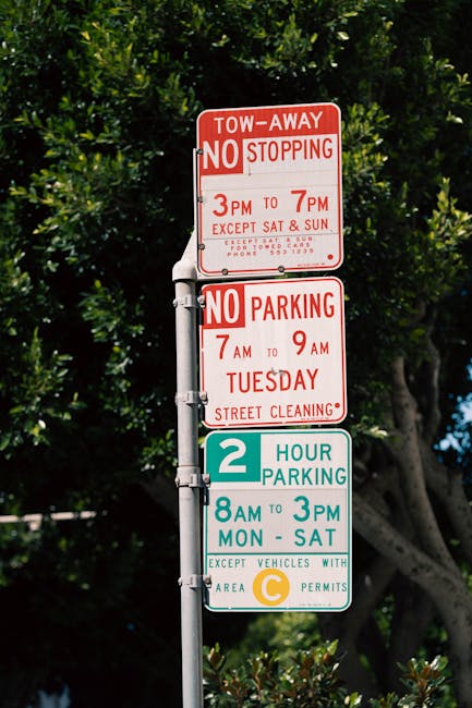 A close-up image of a green and white parking restriction sign mounted on a metal pole set against a blue sky with some clouds. The sign indicates a two-hour parking limit from 8 am to 8 pm, excluding