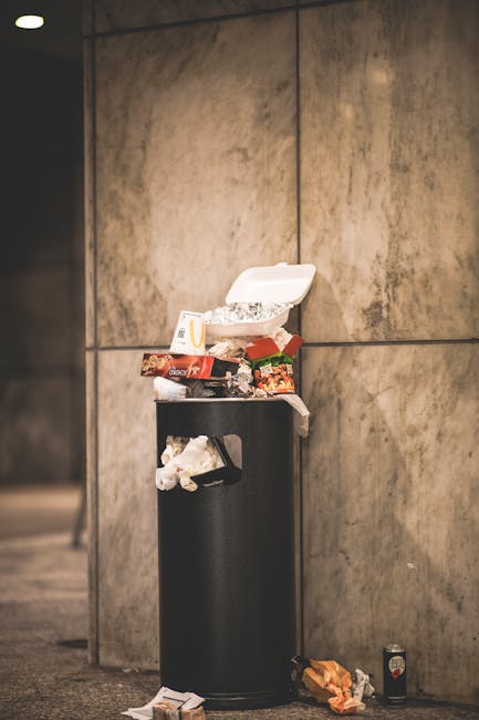 Three large black refuse sacks made of heavy duty plastic, filled with waste, are positioned on a paved sidewalk near the edge of a street. The sacks appear slightly crumpled with some visible creases