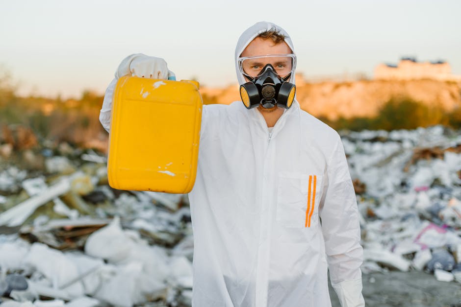 A person wearing orange overalls and white shoes is standing indoors on a grey concrete floor, holding two large blue rubbish bags filled with waste, with one bag in each hand. The bags appear to be m